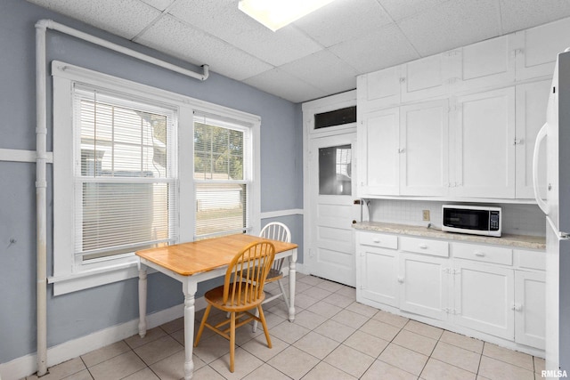 kitchen featuring white appliances, white cabinetry, a paneled ceiling, decorative backsplash, and light tile patterned floors