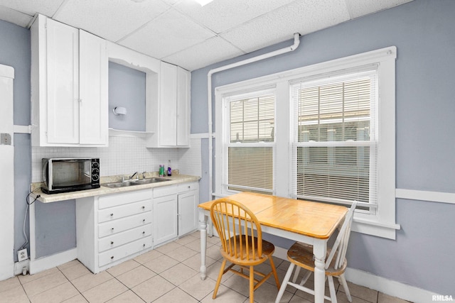 kitchen with sink, light tile patterned flooring, white cabinetry, a paneled ceiling, and tasteful backsplash