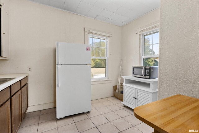 kitchen with white fridge, sink, light tile patterned floors, and a wealth of natural light