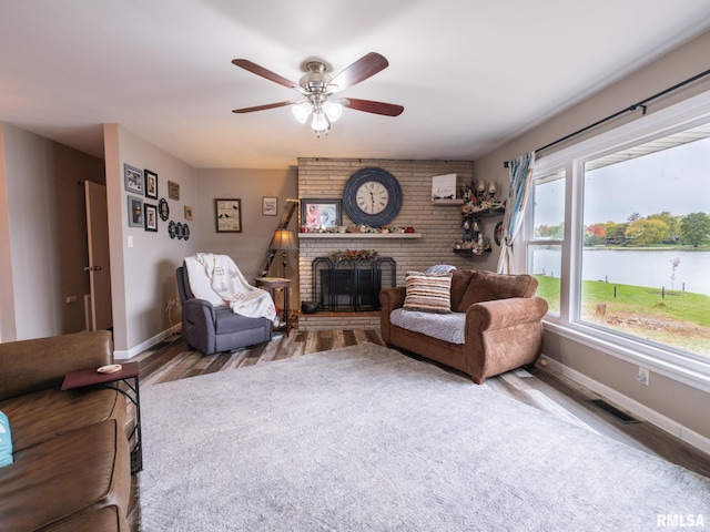 living room with a water view, ceiling fan, wood-type flooring, and a brick fireplace