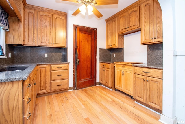 kitchen with ceiling fan, backsplash, dark stone counters, light hardwood / wood-style flooring, and sink