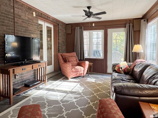 living room featuring french doors, wooden walls, brick wall, crown molding, and ceiling fan