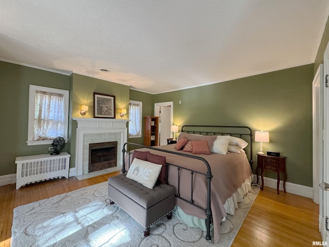 bedroom with crown molding, a fireplace, radiator heating unit, and light hardwood / wood-style floors