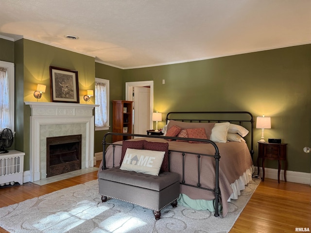 bedroom featuring ornamental molding, light hardwood / wood-style flooring, and a tiled fireplace