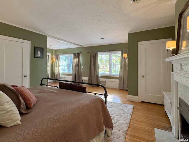 bedroom with light hardwood / wood-style floors, a textured ceiling, ornamental molding, and a tile fireplace