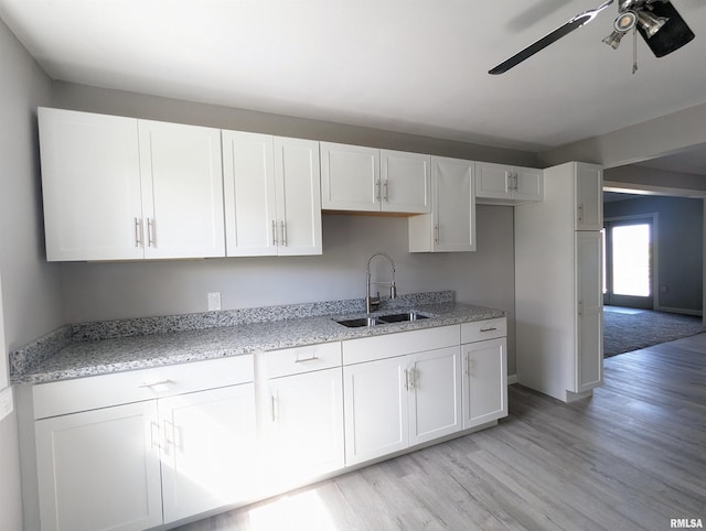 kitchen with light stone countertops, light wood-style flooring, white cabinetry, and a sink