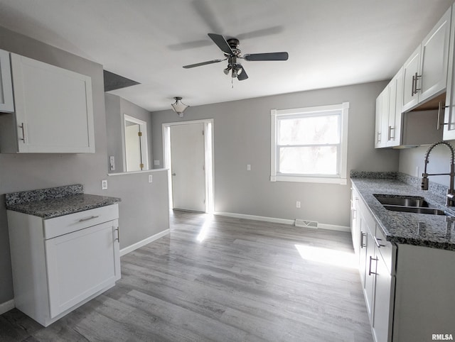 kitchen featuring visible vents, a sink, light wood finished floors, and dark stone countertops