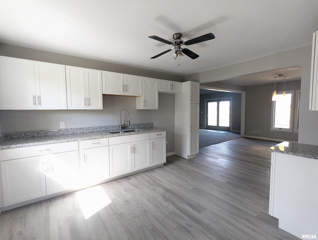 kitchen with light wood-style flooring, white cabinetry, ceiling fan, a sink, and light stone countertops