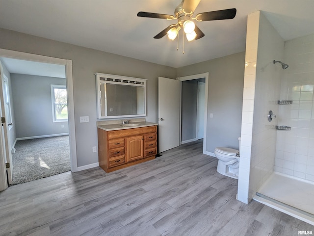 bathroom featuring baseboards, toilet, wood finished floors, a tile shower, and vanity