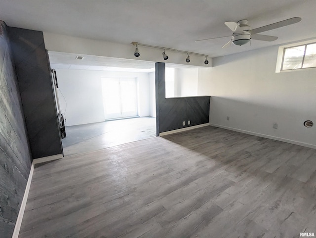 empty room with a ceiling fan, rail lighting, baseboards, and wood finished floors