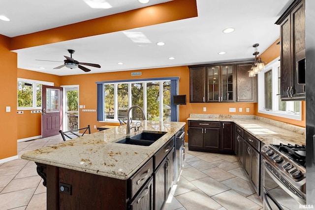 kitchen with a breakfast bar area, an island with sink, sink, light stone countertops, and appliances with stainless steel finishes