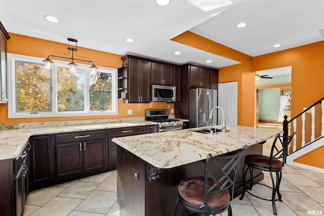 kitchen featuring a kitchen island with sink, hanging light fixtures, stainless steel appliances, sink, and a kitchen bar