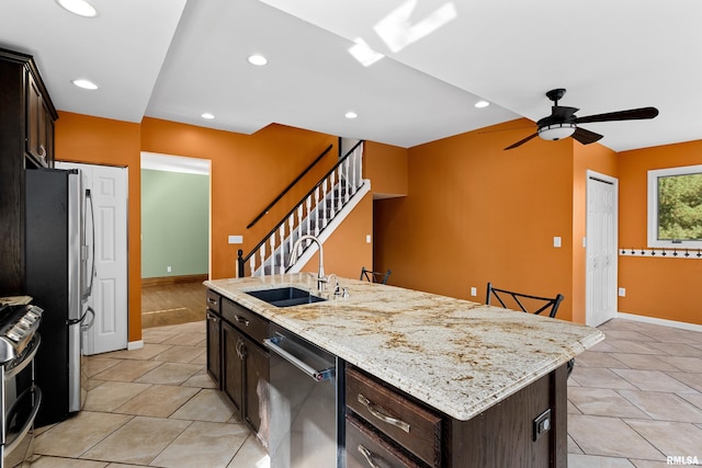 kitchen featuring a kitchen island with sink, a breakfast bar area, dark brown cabinets, light stone countertops, and appliances with stainless steel finishes