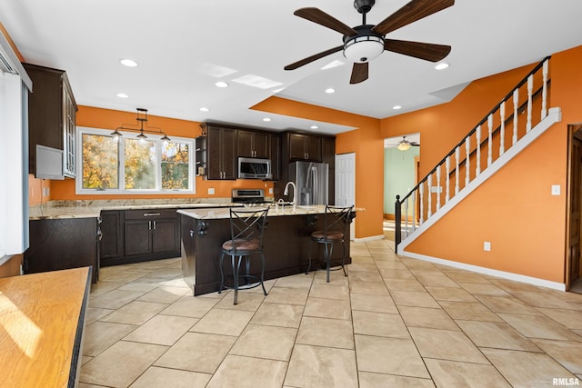 kitchen with a kitchen breakfast bar, a center island with sink, decorative light fixtures, light tile patterned floors, and appliances with stainless steel finishes