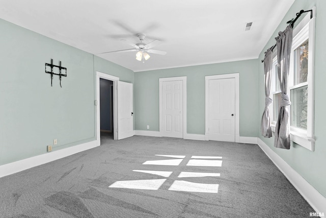 unfurnished bedroom with ceiling fan, multiple closets, and carpet floors