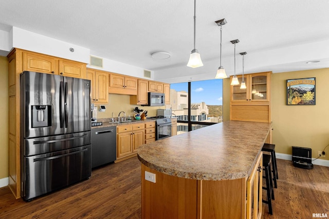 kitchen featuring a kitchen breakfast bar, hanging light fixtures, stainless steel appliances, sink, and dark hardwood / wood-style flooring