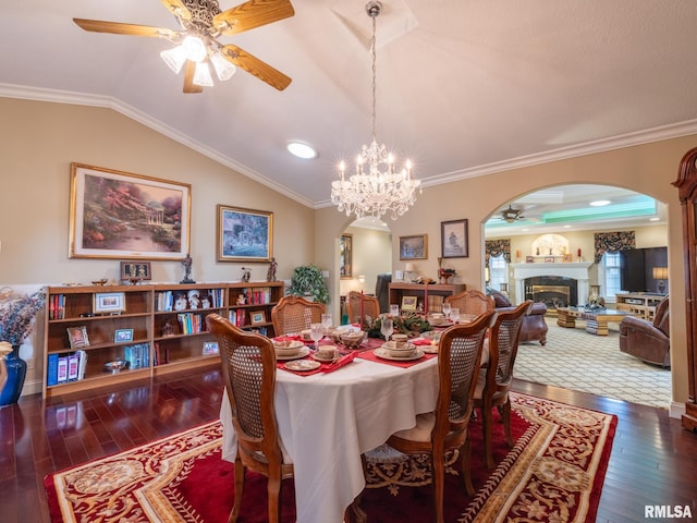 dining area with crown molding, ceiling fan with notable chandelier, dark wood-type flooring, and vaulted ceiling