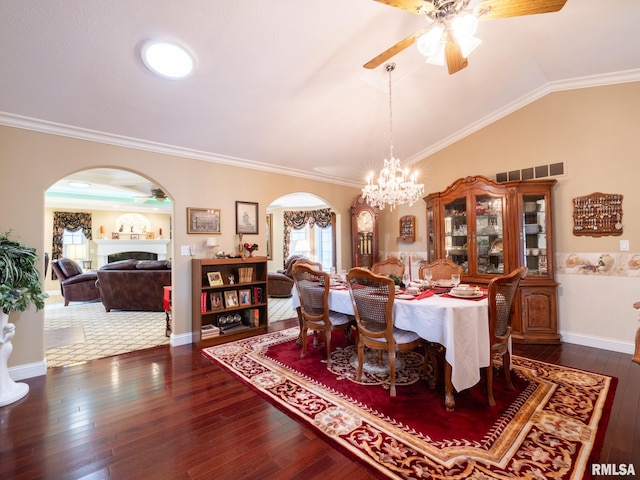 dining area featuring ornamental molding, ceiling fan with notable chandelier, vaulted ceiling, and dark wood-type flooring