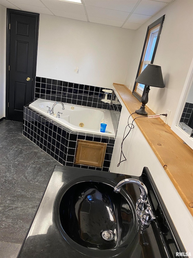 bathroom featuring a relaxing tiled tub and a drop ceiling