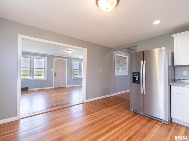 kitchen featuring light wood-type flooring, stainless steel fridge with ice dispenser, light stone counters, and white cabinets