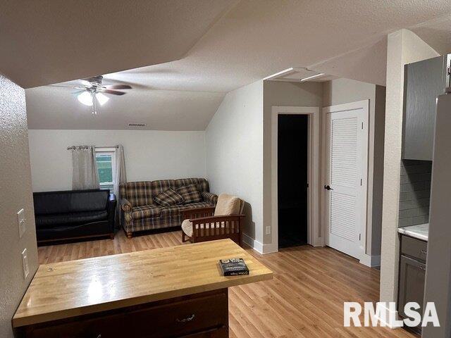 living room with light hardwood / wood-style flooring, ceiling fan, and vaulted ceiling