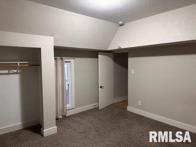 unfurnished bedroom featuring dark colored carpet, vaulted ceiling, and a textured ceiling