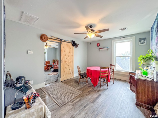 dining space with a barn door, light wood-type flooring, and ceiling fan