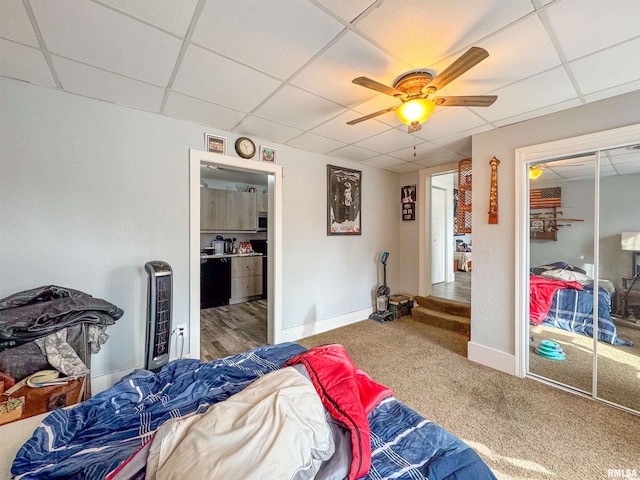 carpeted bedroom with a closet, ceiling fan, heating unit, and a drop ceiling