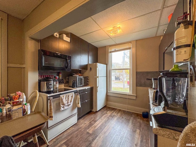 kitchen featuring a drop ceiling, dark brown cabinetry, dark wood-type flooring, and white appliances