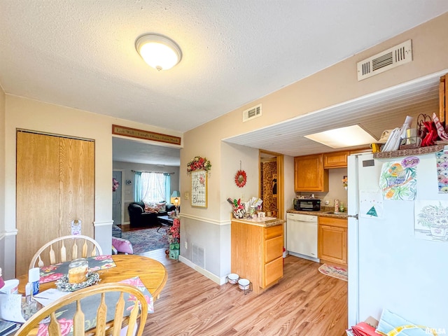 kitchen with a textured ceiling, sink, white appliances, and light wood-type flooring