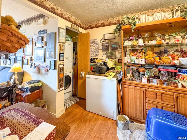 laundry room with stacked washer and clothes dryer, a textured ceiling, and light wood-type flooring