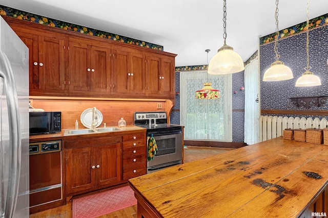 kitchen with wood counters, appliances with stainless steel finishes, light wood-type flooring, sink, and hanging light fixtures