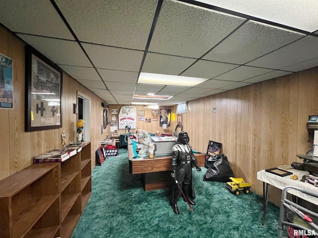 recreation room featuring a paneled ceiling, wooden walls, and dark carpet