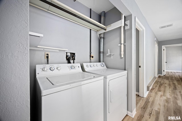 clothes washing area with washing machine and clothes dryer and light wood-type flooring