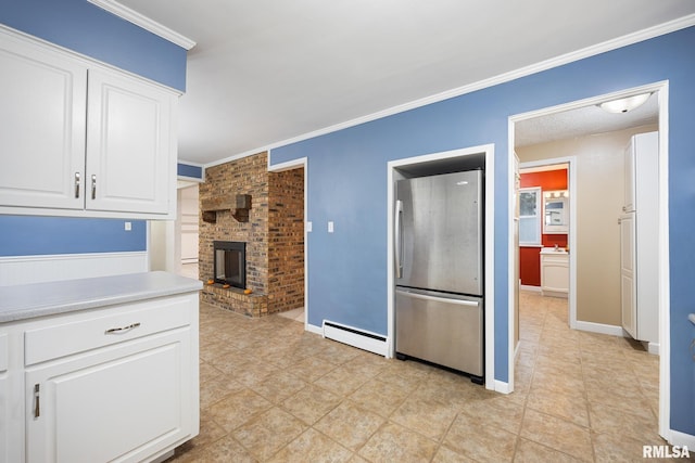 kitchen featuring baseboard heating, a fireplace, crown molding, white cabinets, and stainless steel fridge