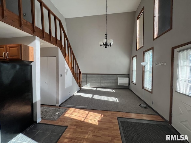 foyer entrance with a chandelier, dark wood-type flooring, a towering ceiling, stairs, and a wall mounted AC