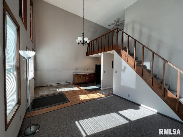 interior space with ceiling fan with notable chandelier, a high ceiling, baseboard heating, and a healthy amount of sunlight