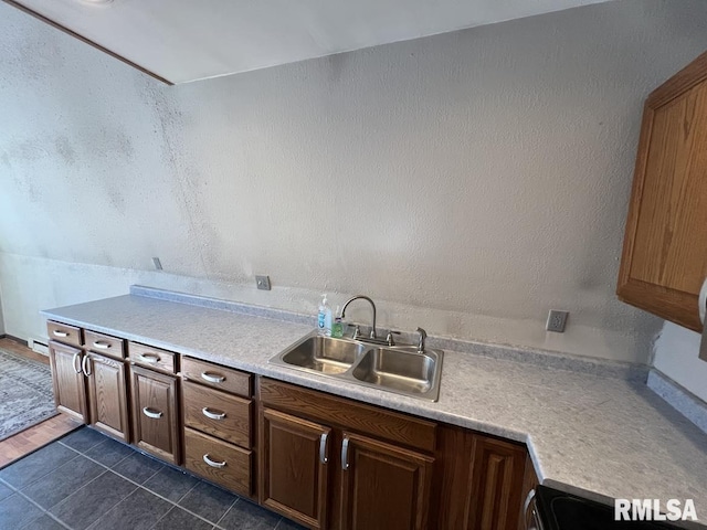 kitchen with brown cabinets, a textured wall, light countertops, and a sink