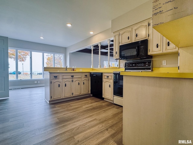 kitchen with kitchen peninsula, hardwood / wood-style floors, black appliances, and sink