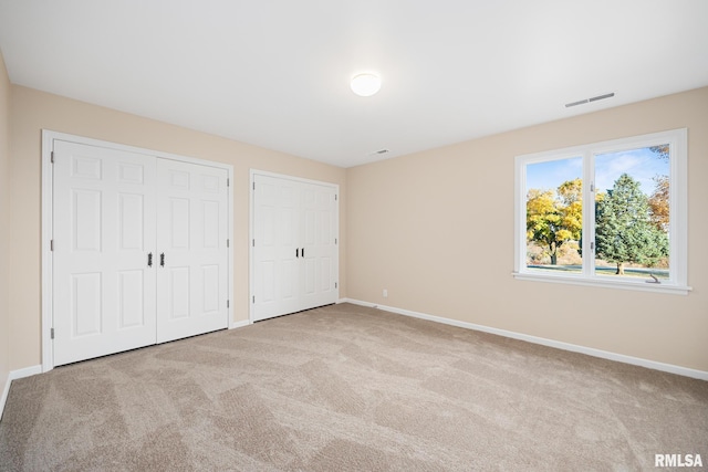 unfurnished bedroom with two closets and light colored carpet