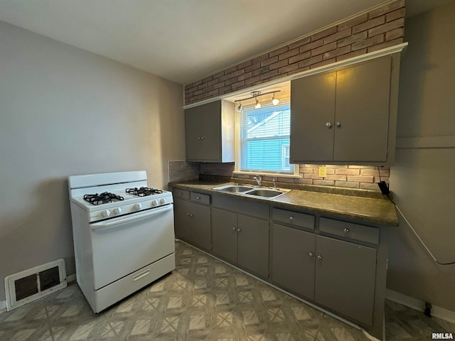 kitchen with gray cabinets, white gas range, sink, and backsplash