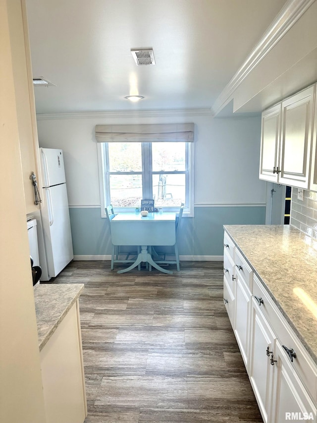 kitchen with white cabinets, light stone counters, backsplash, and white refrigerator