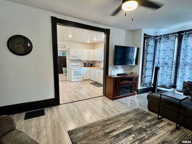 living room with a textured ceiling, light wood-type flooring, and ceiling fan