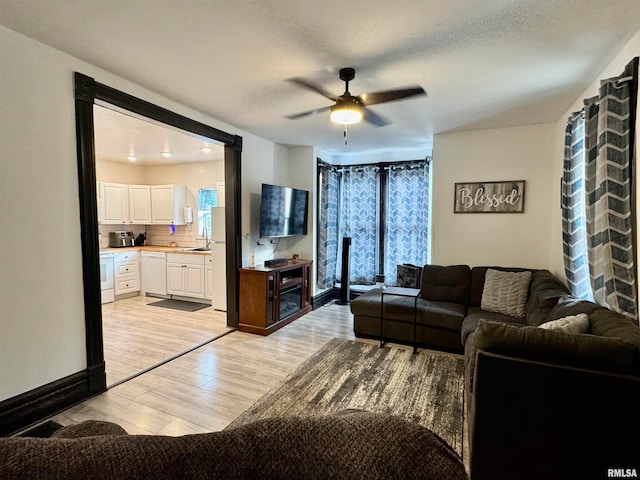 living room featuring sink, light hardwood / wood-style flooring, a textured ceiling, and ceiling fan