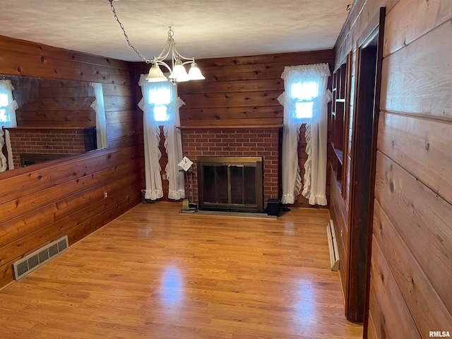 unfurnished living room with wood walls, wood-type flooring, a fireplace, and a baseboard heating unit