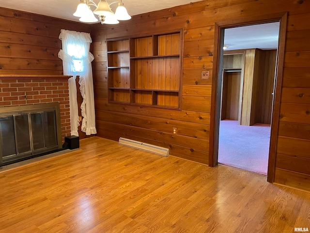 unfurnished living room featuring light hardwood / wood-style floors, a fireplace, wood walls, and a baseboard heating unit