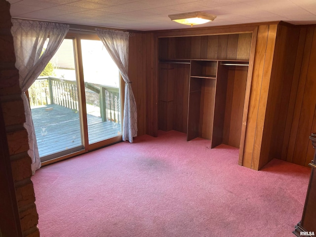 unfurnished bedroom featuring light carpet, a closet, wood walls, and access to outside