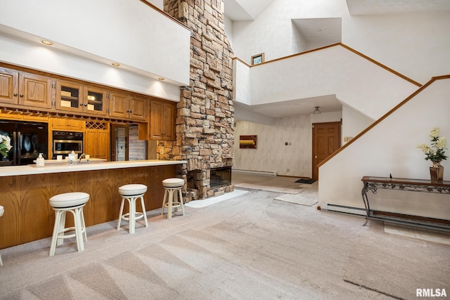 kitchen featuring kitchen peninsula, a breakfast bar, black appliances, light colored carpet, and a towering ceiling