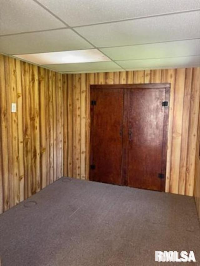 unfurnished room featuring a paneled ceiling, carpet, and wooden walls