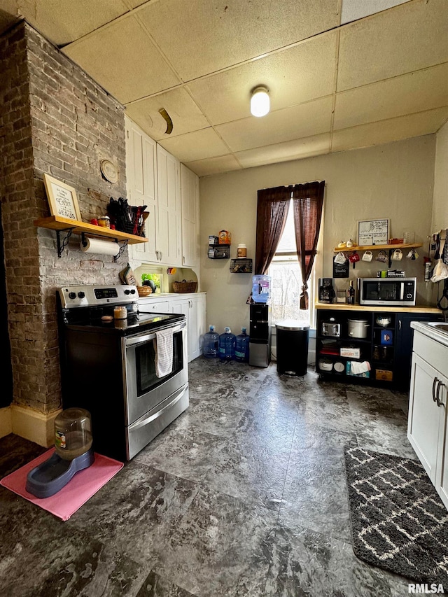 kitchen with brick wall, white cabinetry, a paneled ceiling, and stainless steel electric range oven